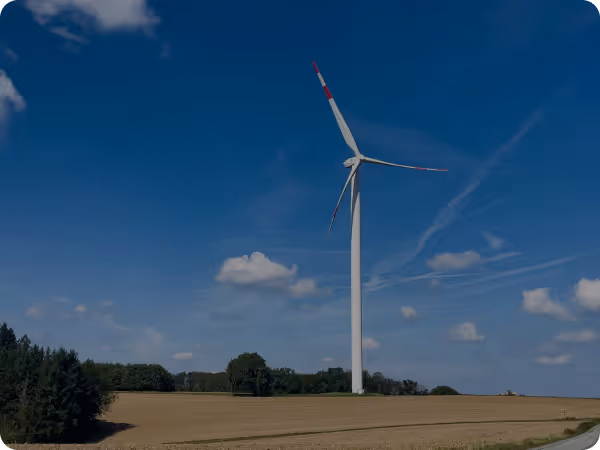 Wind turbine standing in an open field under a blue sky with scattered clouds.