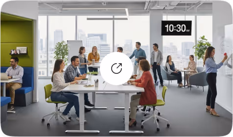 An open office space with employees collaborating at tables, engaged in discussions, and working on presentations. A large clock on the wall shows 10:30 AM, and large windows provide a view of the city skyline.