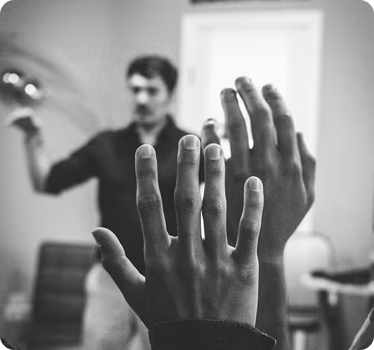 Hands raised in defense against a man swinging an object in the background.