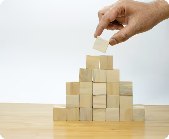 Hand placing wooden block on top of stacked wooden blocks forming a pyramid structure.