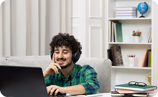 Man wearing headset sits at desk with laptop, books, and globe on shelf in background.