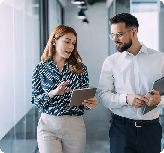 Business colleagues discuss data on digital tablet and laptop in modern office hallway setting together.