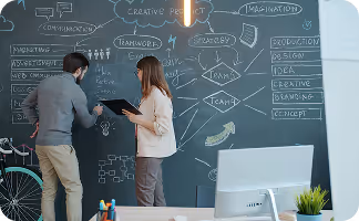Two professionals collaborating on a blackboard with business strategy and marketing concepts written on wall.