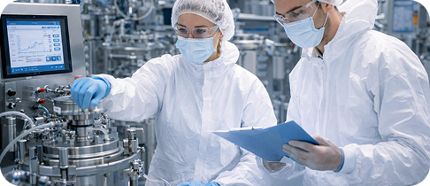 A young man with curly hair wearing headphones sits on a sofa, smiling while working on a laptop. A bookshelf with books and decor is visible in the background.