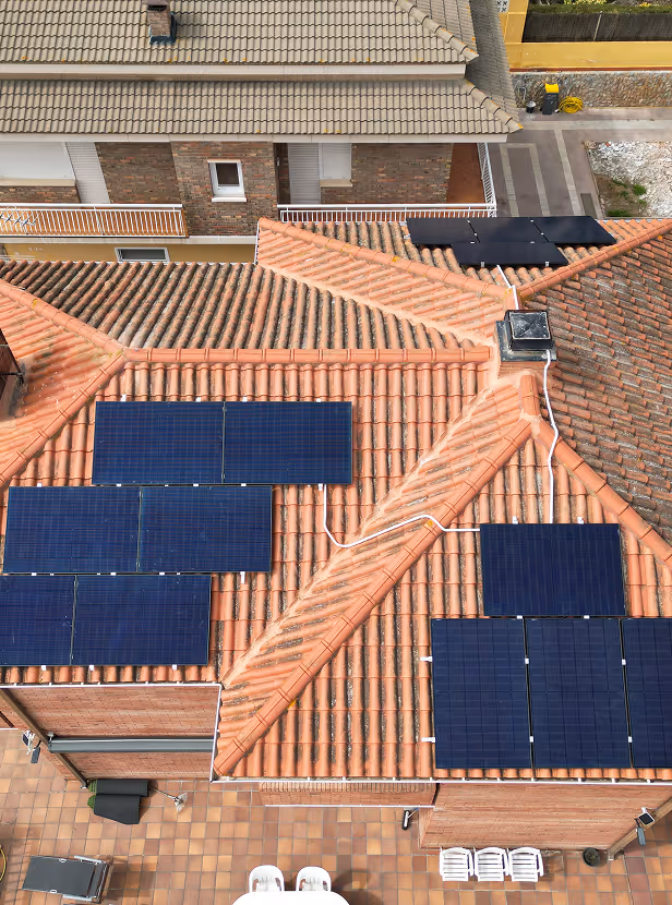 Paneles solares instalados sobre un techo de tejas rojas en una casa residencial vista desde arriba.