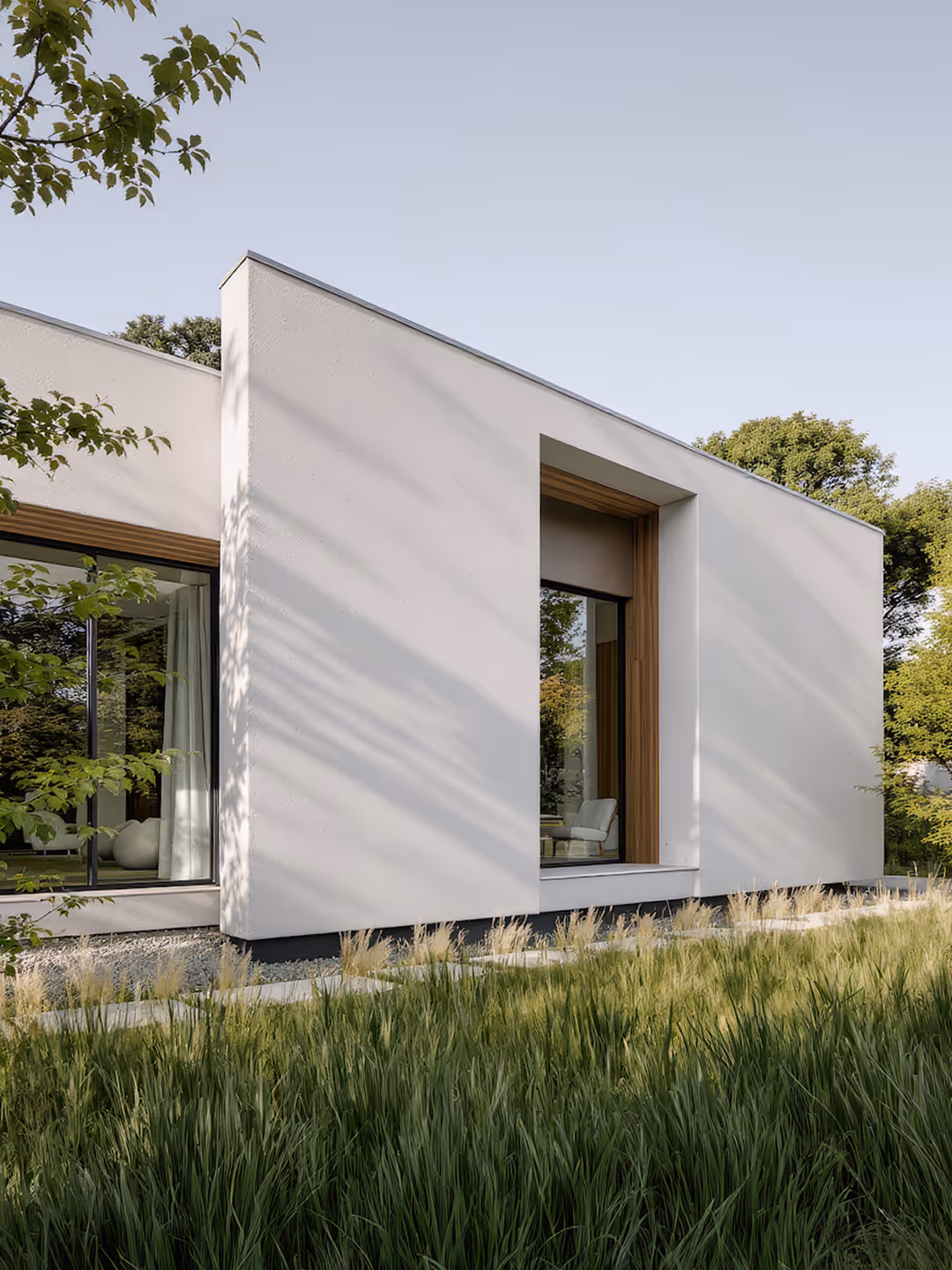 Casa moderna blanca con grandes ventanas y jardín con hierba alta.