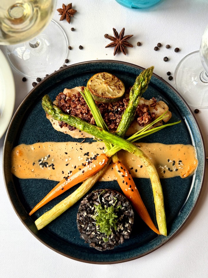 Elegante Telleranrichtung mit gegrilltem Hähnchen, gebratenem Spargel, Mini-Karotten, einer Zitronenscheibe, Sauce und schwarzem Reis mit Kresse garniert.