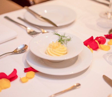 Elegante weiße Serviette mit Butter in einer kleinen Schale, garniert mit Dill, auf einem weiß gedeckten Tisch mit Rosenblättern und Besteck.