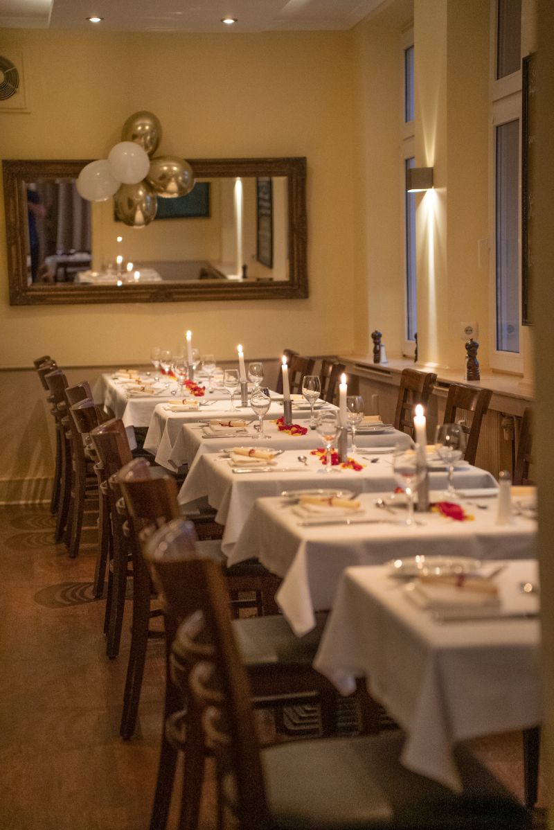 Elegantes Restaurant mit eingedeckten Tischen, weißen Tischdecken, Kerzenlicht und Holzstühlen.