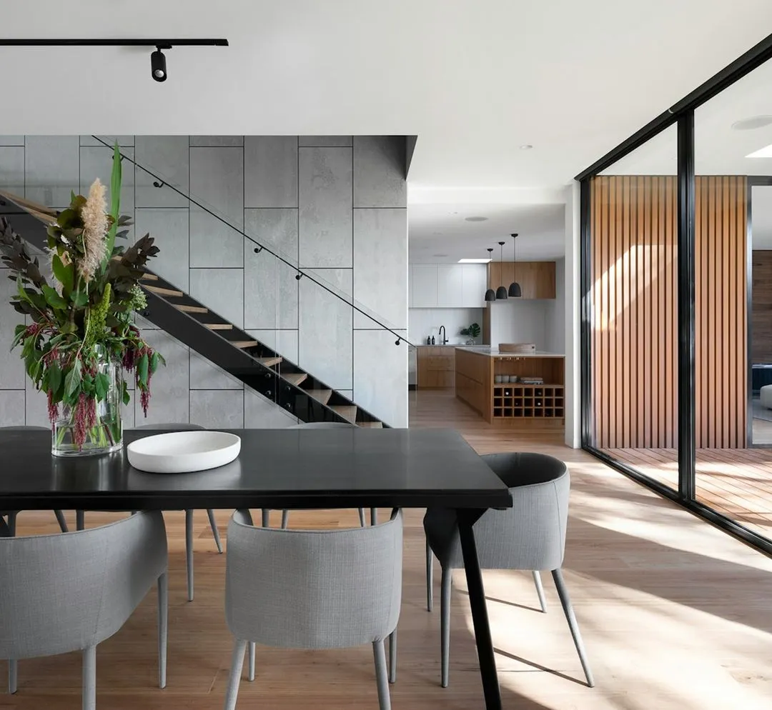 Intérieur moderne avec salle à manger, escalier en métal et cuisine ouverte en arrière-plan.