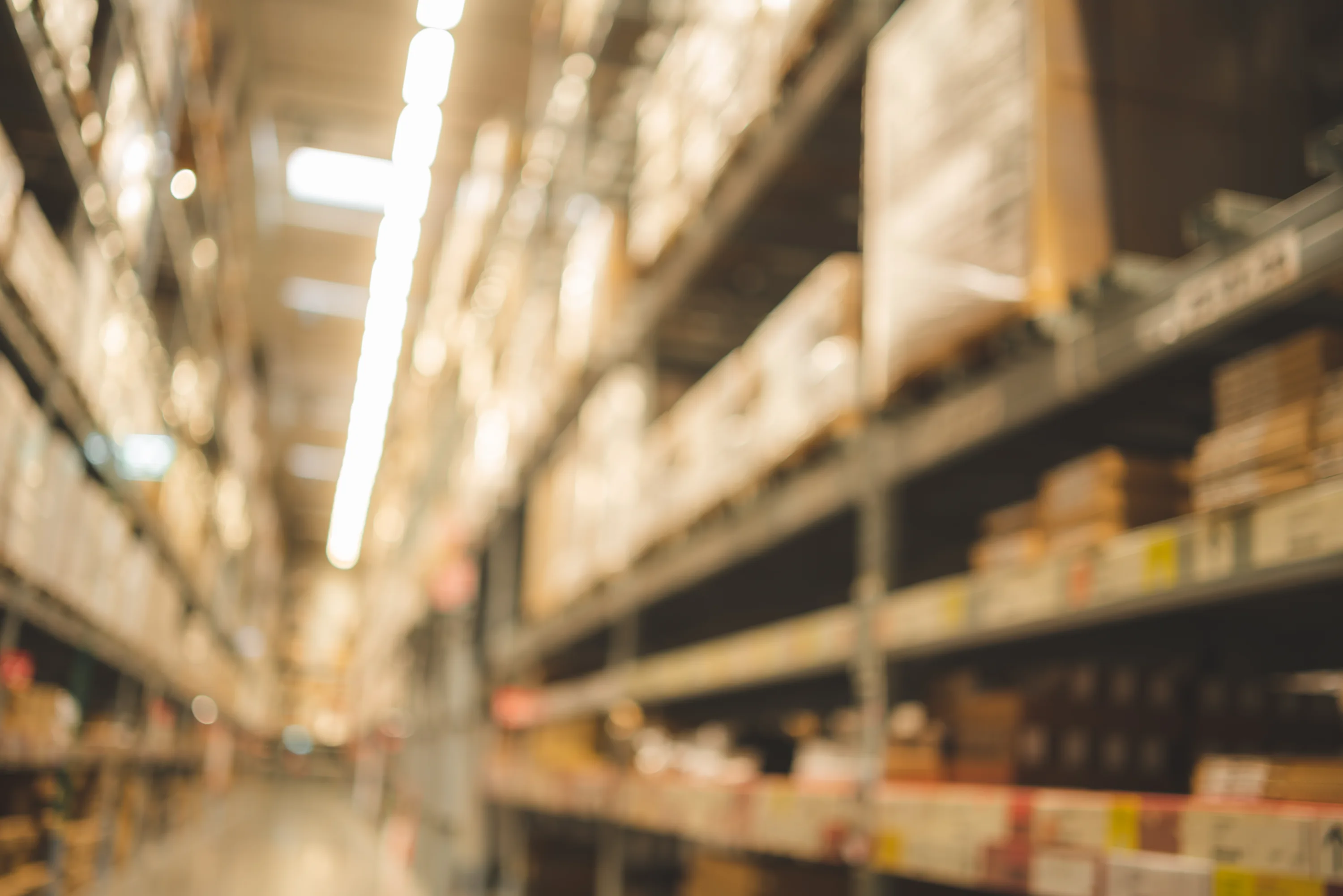 Blurry view of a warehouse aisle with shelves stocked with boxes and goods.