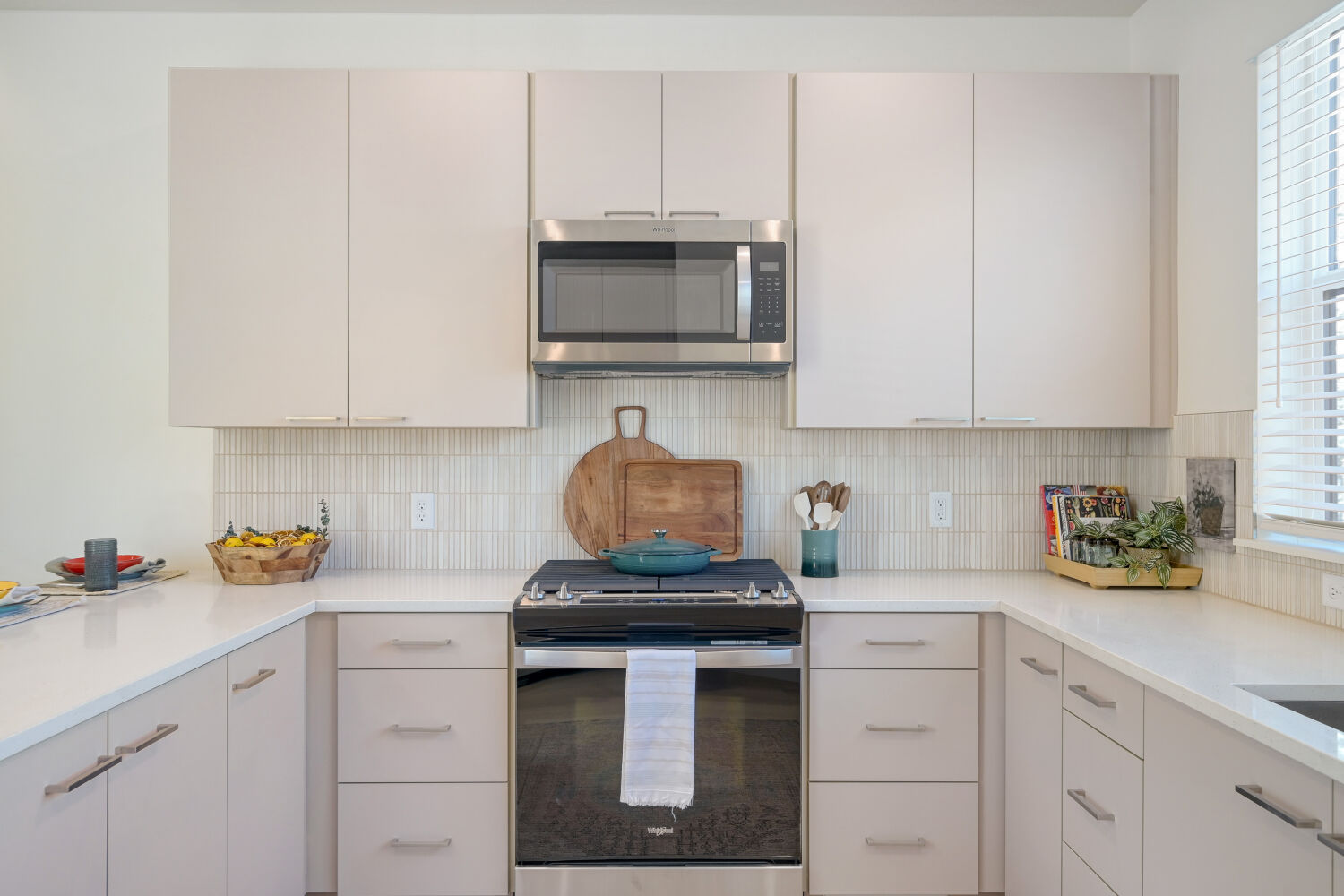 View of Townhouse kitchen featuring sink by large window, white cabinets, and stainless steel appliances