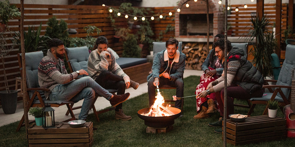 Friends roast marshmallows, chat and laugh as they spend time relaxing by the backyard fire ring. A fire pit is a great way to enjoy your outdoor space and can often be used on warm and even cooler nights, weather permitting.