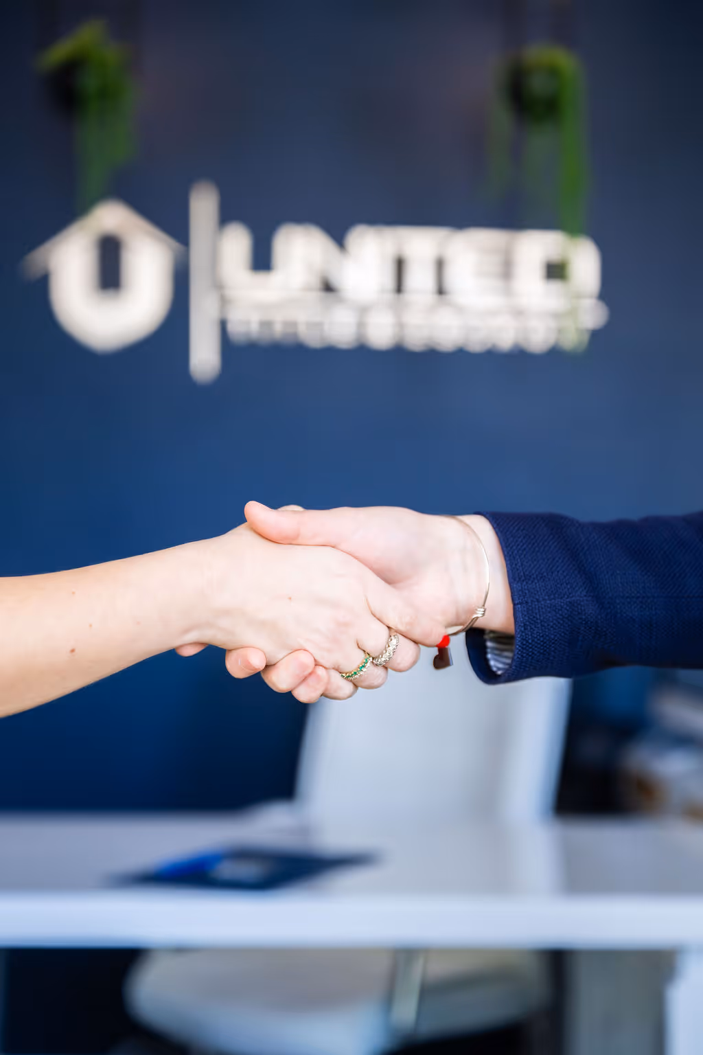 Two people shaking hands in front of a blurred UNITEDTITLE sign on a blue wall.