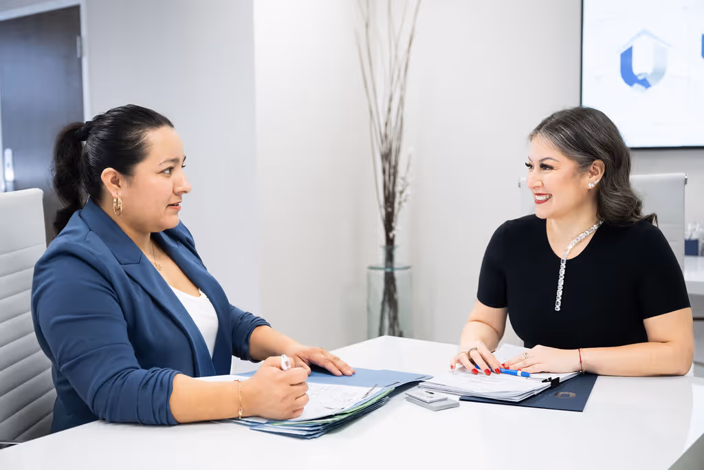 Two professional women in an office having a discussion over documents at a white table.