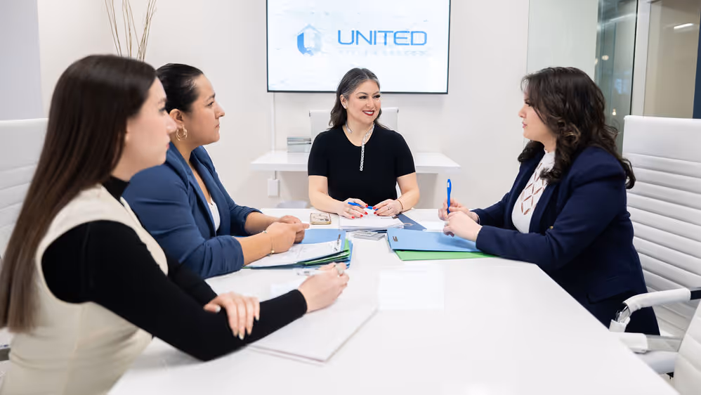 Four professional women seated around a white conference table in a meeting room with a screen displaying the United Title Escrow logo.