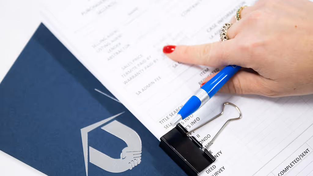 Close-up of a hand holding a pen pointing at a document with text and a black binder clip on a dark blue folder with the United Title logo.