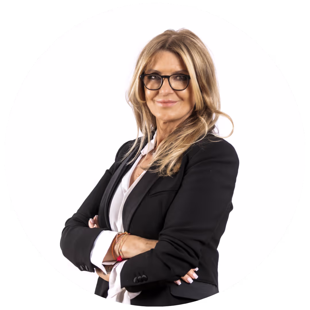 Femme blonde portant des lunettes, veste noire et chemise blanche, bras croisés, souriant.