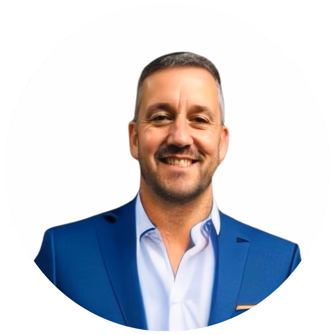 Homme souriant portant un costume bleu et une chemise blanche sur fond blanc.