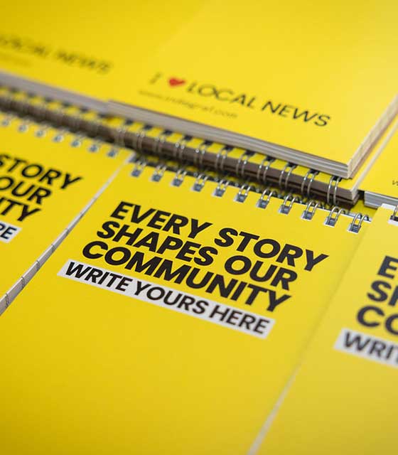 Indiegraf's swag, yellow spiral notebooks with the text 'EVERY STORY SHAPES OUR COMMUNITY WRITE YOURS HERE' on their covers.