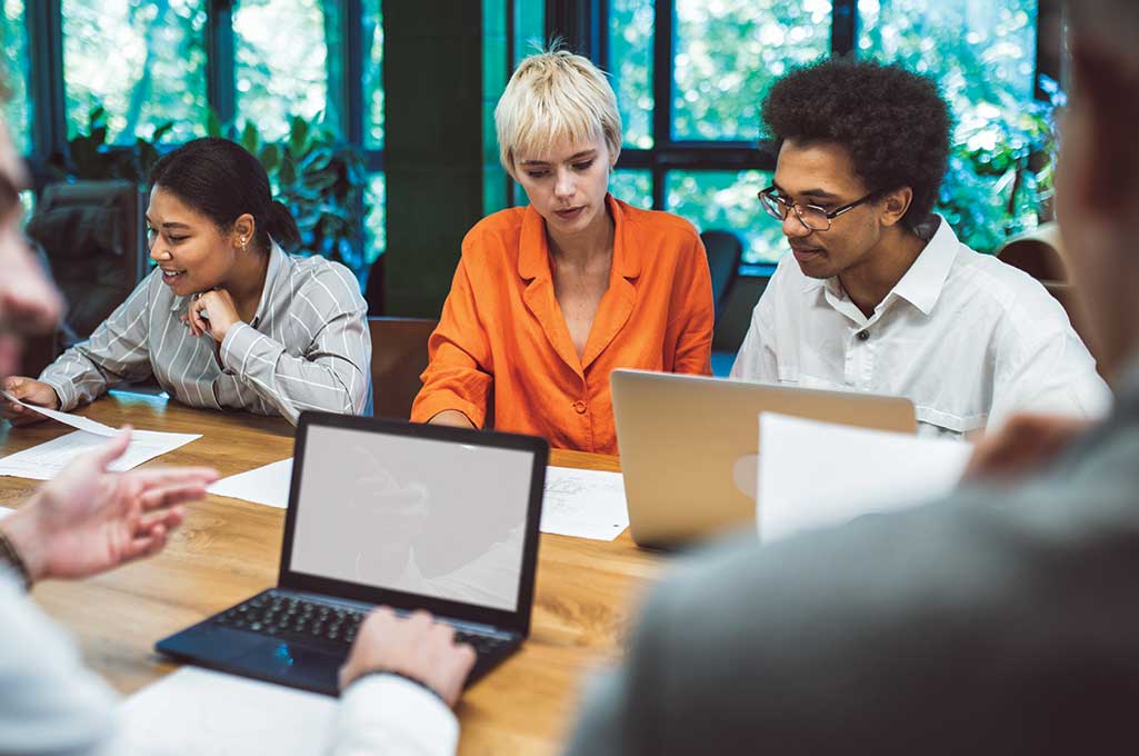 A diverse team of media professionals collaborating on a laptop, illustrating Indiegraf's hands-on newsroom support and strategy.