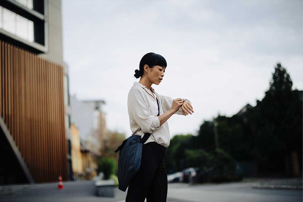 Woman standing outdoors on a city street checking the time on her wristwatch.