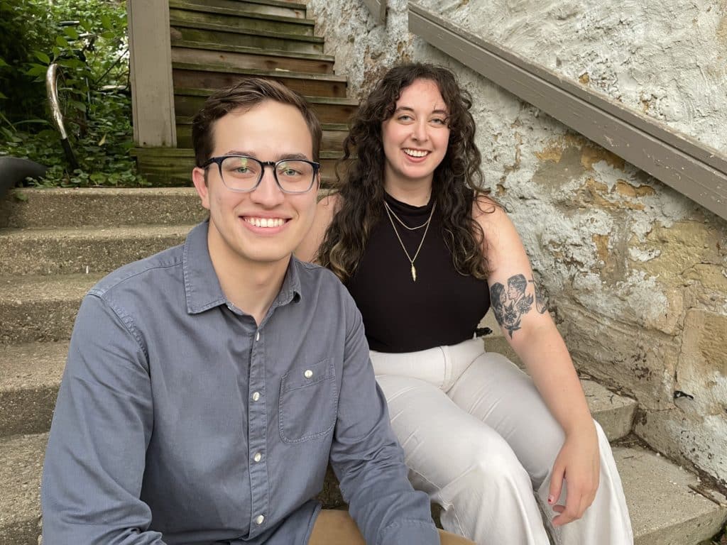 Sam Hoisington and Hayley Sperling sitting on steps. Plants in the background.