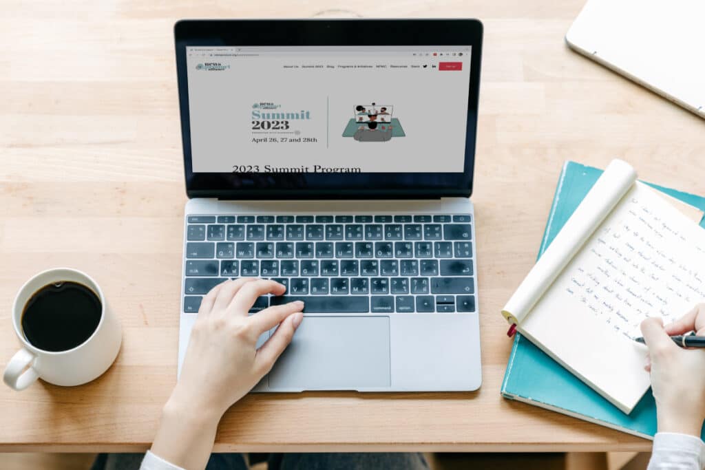 Person at a desk using a laptop and writing notes.