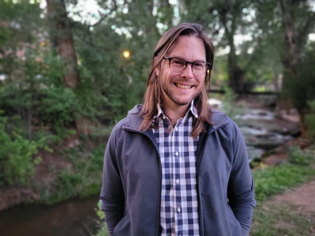 A man wearing a plaid shirt and grey jacket smiling in a forest. What is Indiegraf.