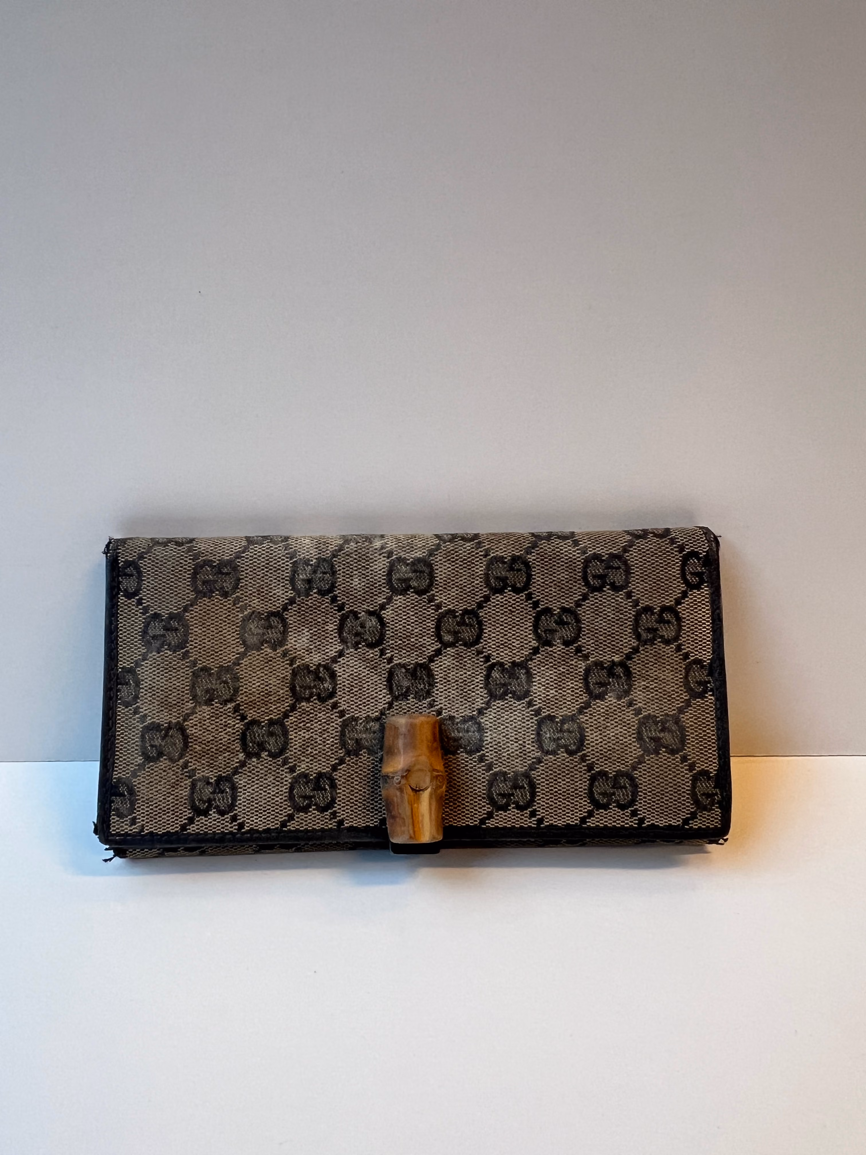 Gucci GG monogram canvas wallet with a bamboo clasp closure, with frayed edges visible on the trim.