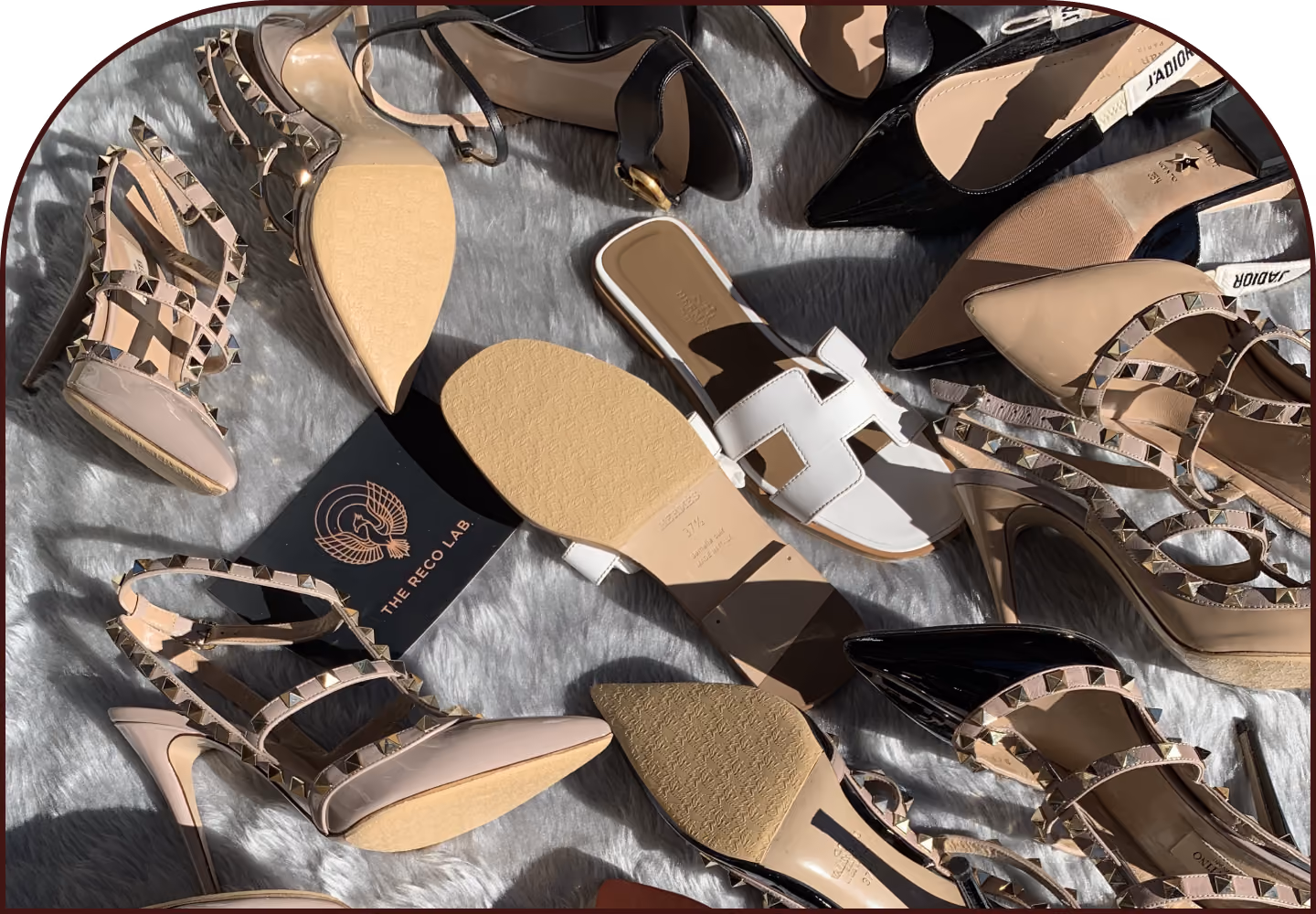 Collection of designer shoes ready for restoration, including Valentino Rockstud heels, Hermès Oran sandals, Dior slingbacks and patent leather pumps, arranged by The Reco Lab.