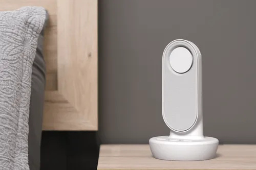 A tall electronic device with an aqua colored light ring at the top sits on a bedside table.