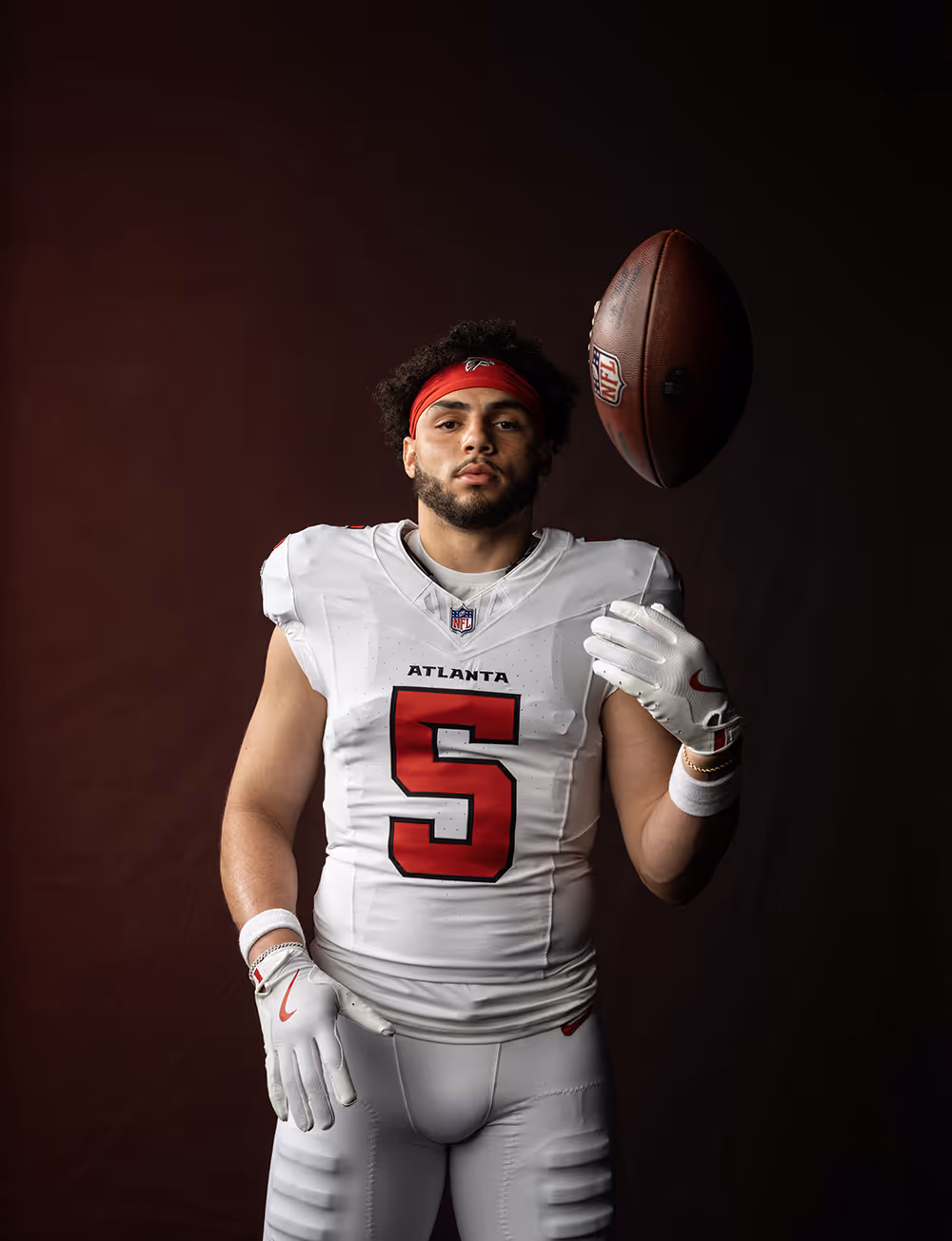 Football player in white Atlanta jersey number 5 spinning a football on his finger against a dark background.