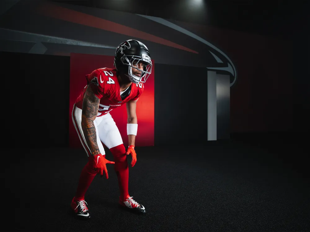 Side profile of a football player wearing red and white Atlanta Falcons uniform holding a black helmet with the team's logo.