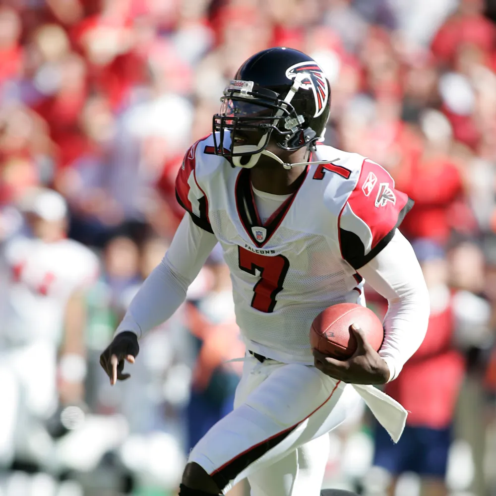 Atlanta Falcons football player, Michael Vick, in white and red uniform holding a football while running on the field.