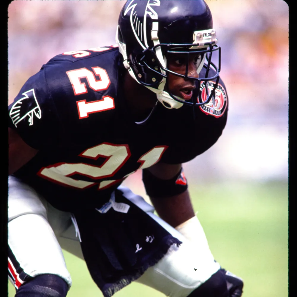 Atlanta Falcons football player in black uniform with number 21 in a ready stance on the field.