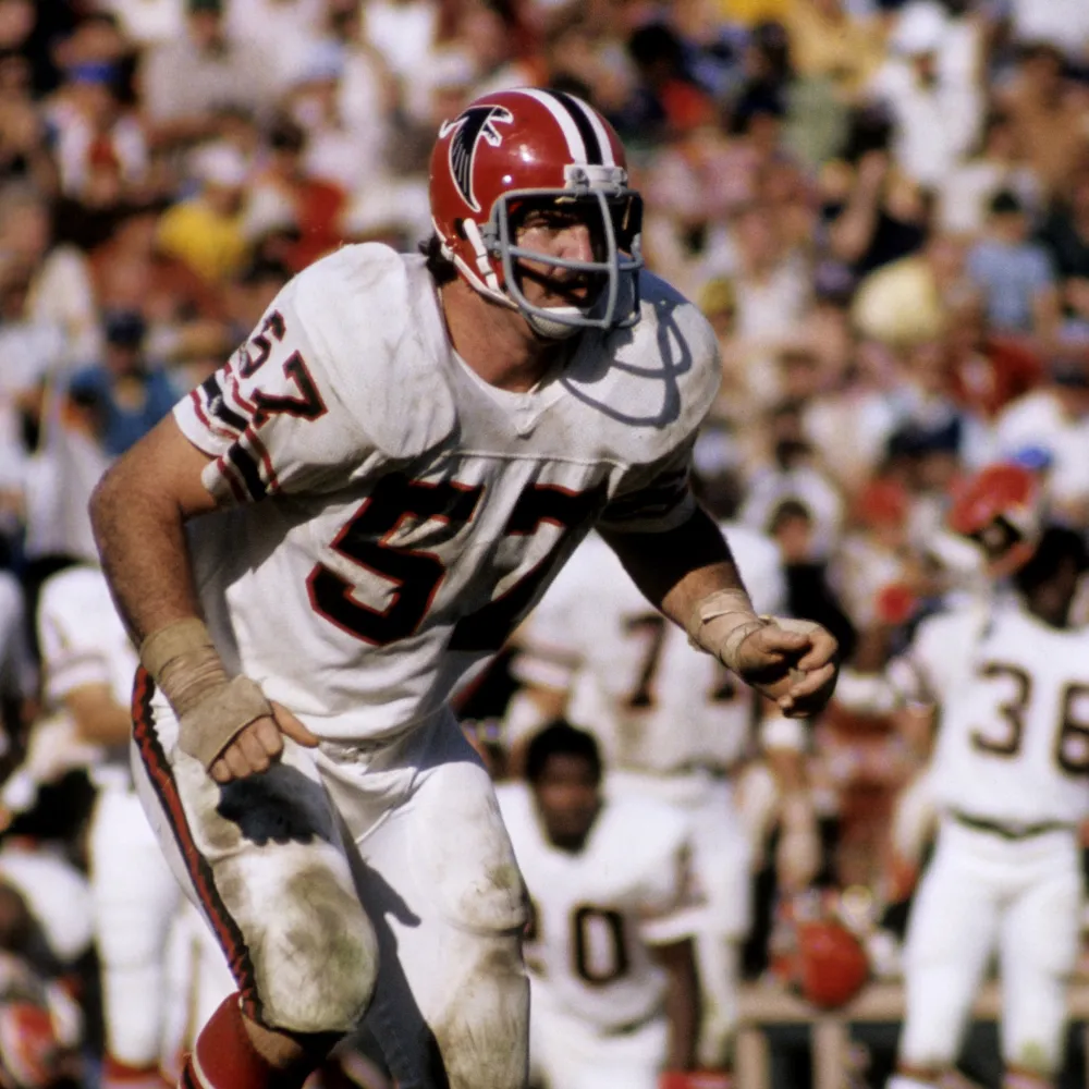 Football player in white uniform with number 57 and red helmet with Falcons logo, running on field during a game.