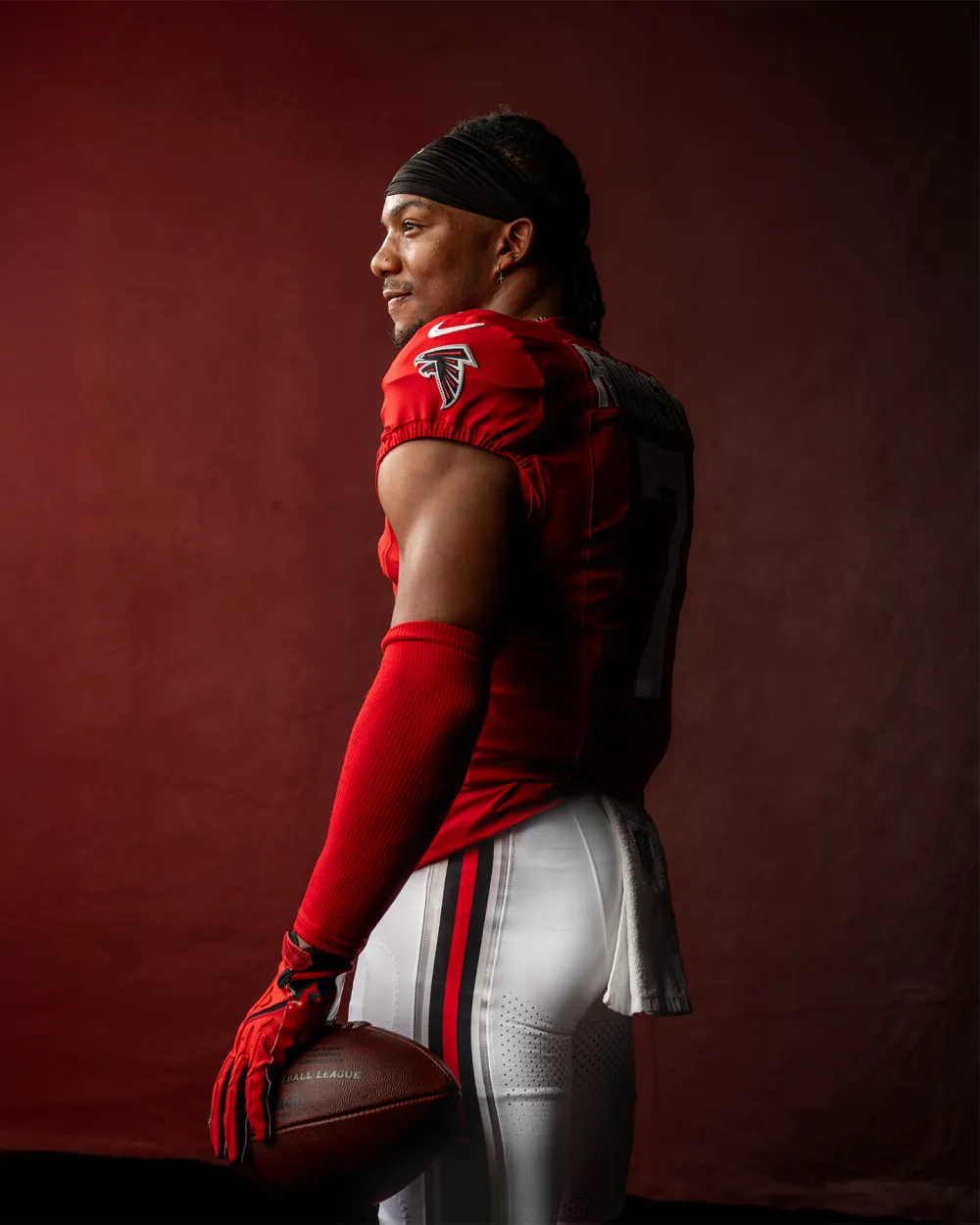 Football player in Atlanta Falcons red home jersey, white pants, red gloves, and helmet running with a football.