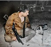 Person in military uniform kneeling on snow while holding a rifle and looking at a German Shepherd dog.