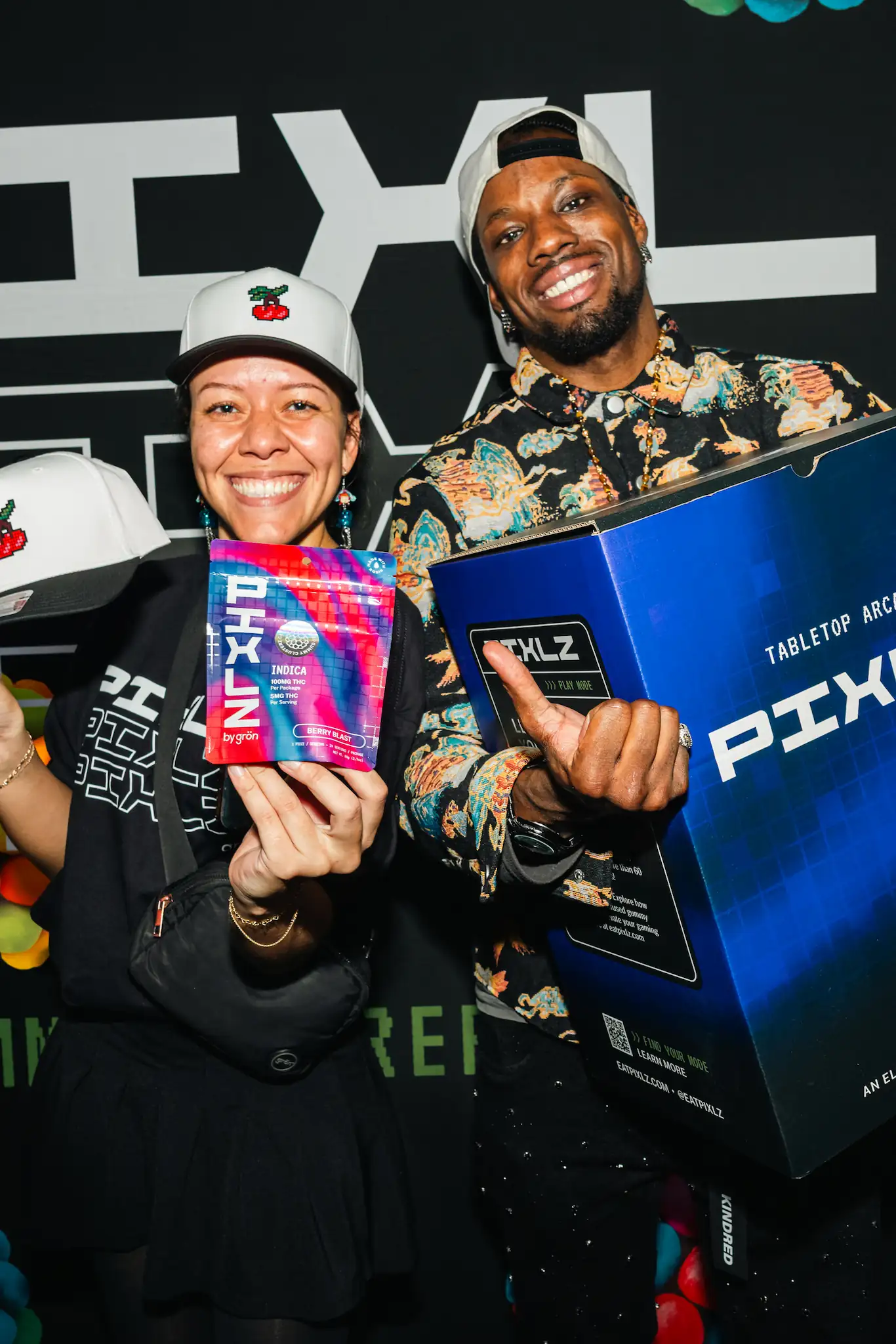 Smiling woman and man holding PIXLZ branded products at an event with black background.