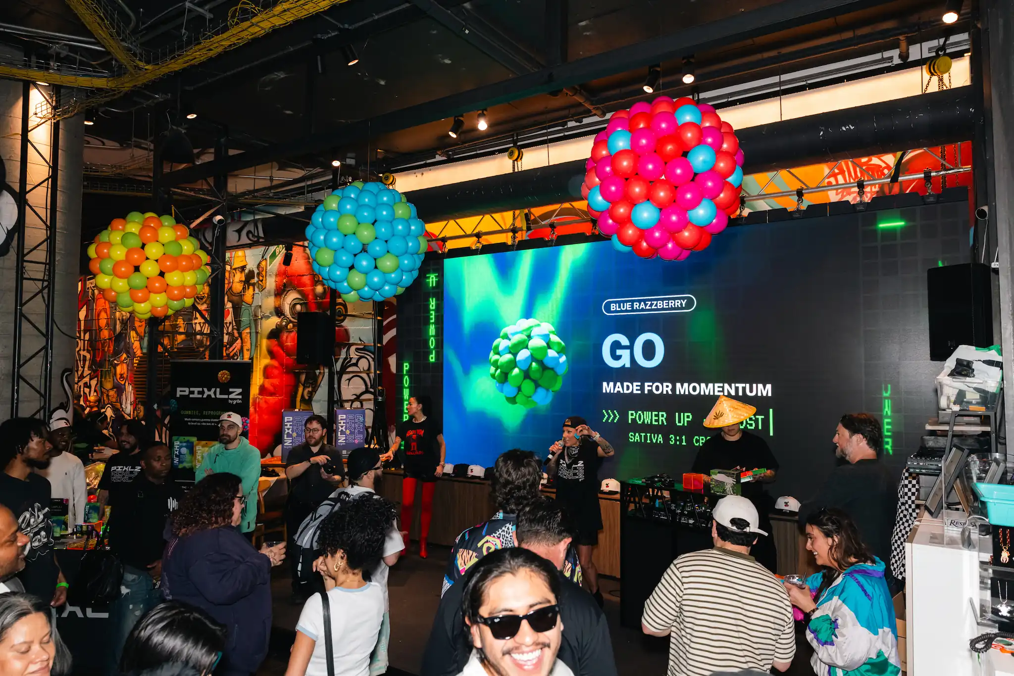 Crowd at event with colorful balloon clusters and a screen displaying 'GO made for momentum' ad.