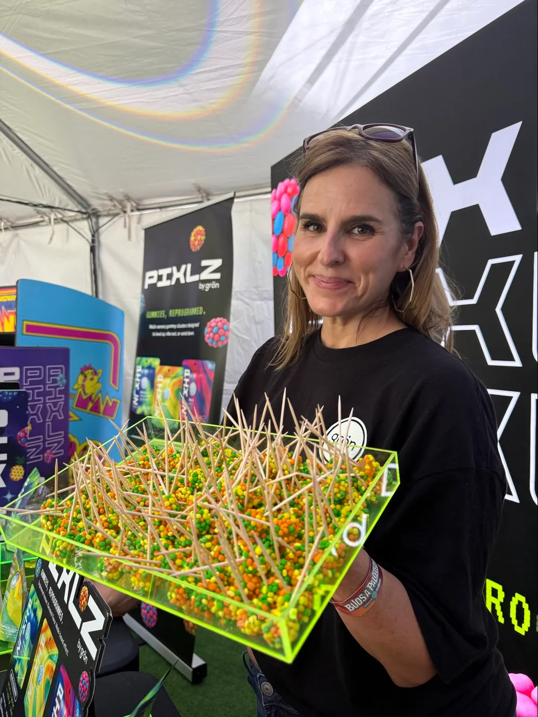 Woman holding a tray of colorful candy samples with toothpicks at a Pixlz branded booth.