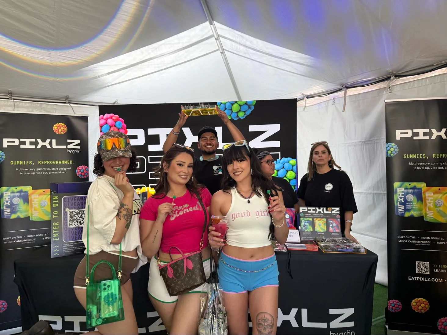 Smiling group of five people posing at Pixlz booth with promotional banners and gummies displayed.