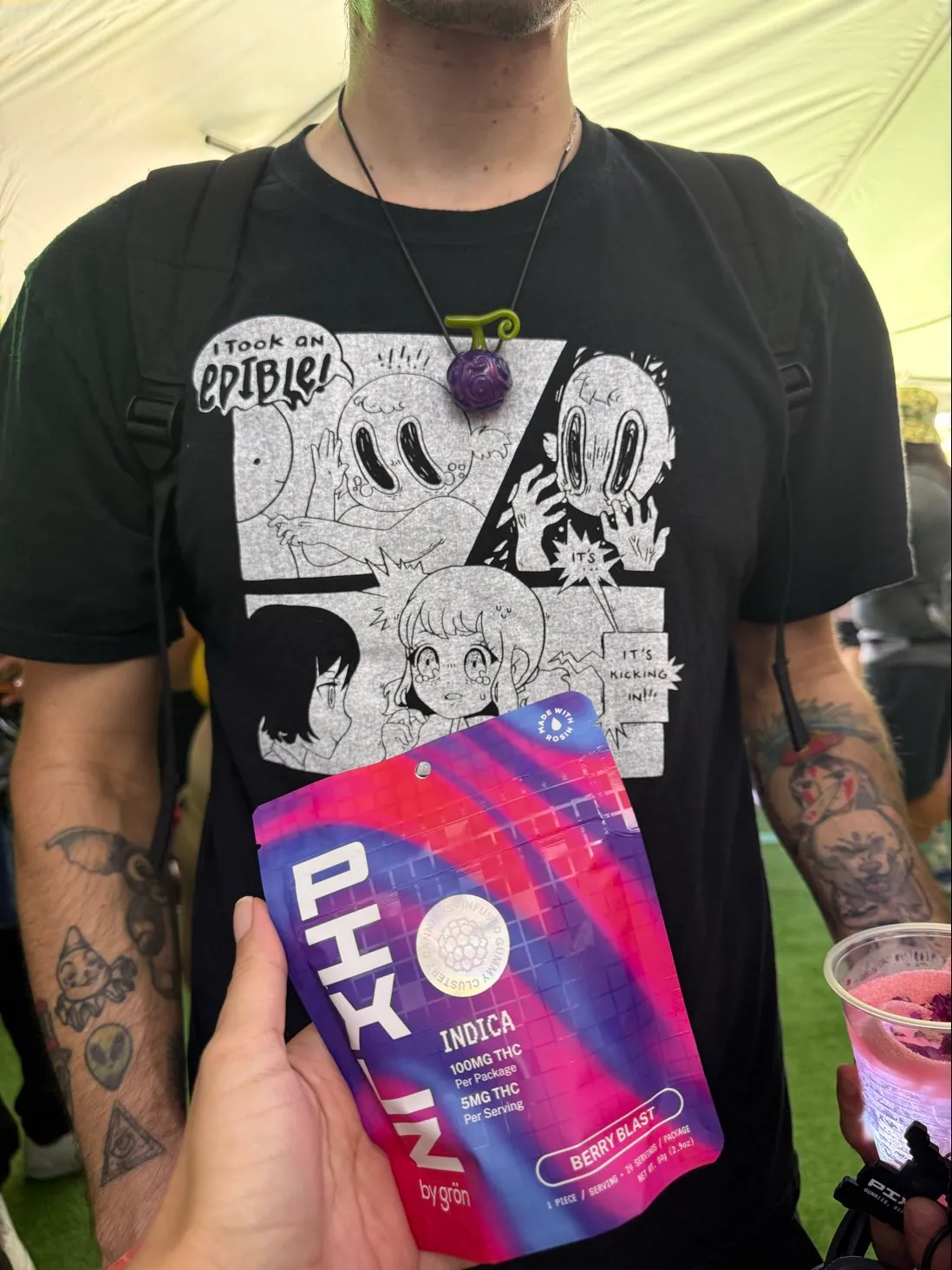 Person wearing black shirt with cartoon print and holding a colorful PIXLZ indica edible package.