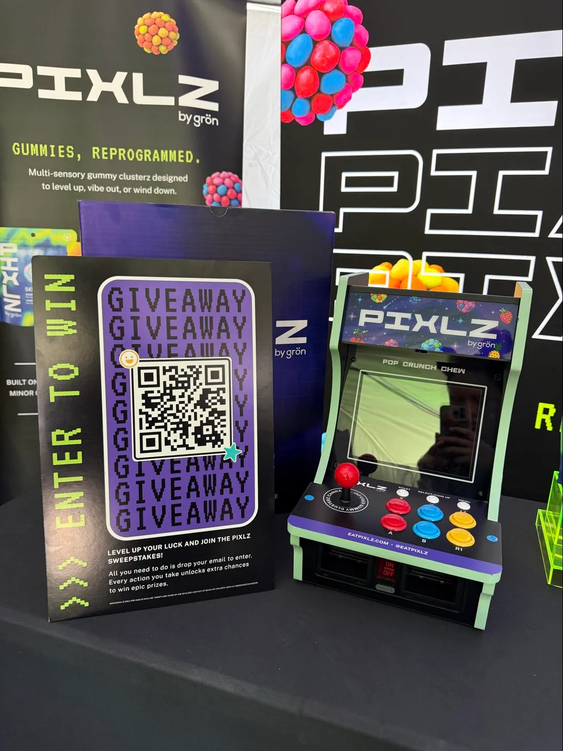 Pixlz arcade game machine with joystick, buttons, and a QR code giveaway sign on a black table.