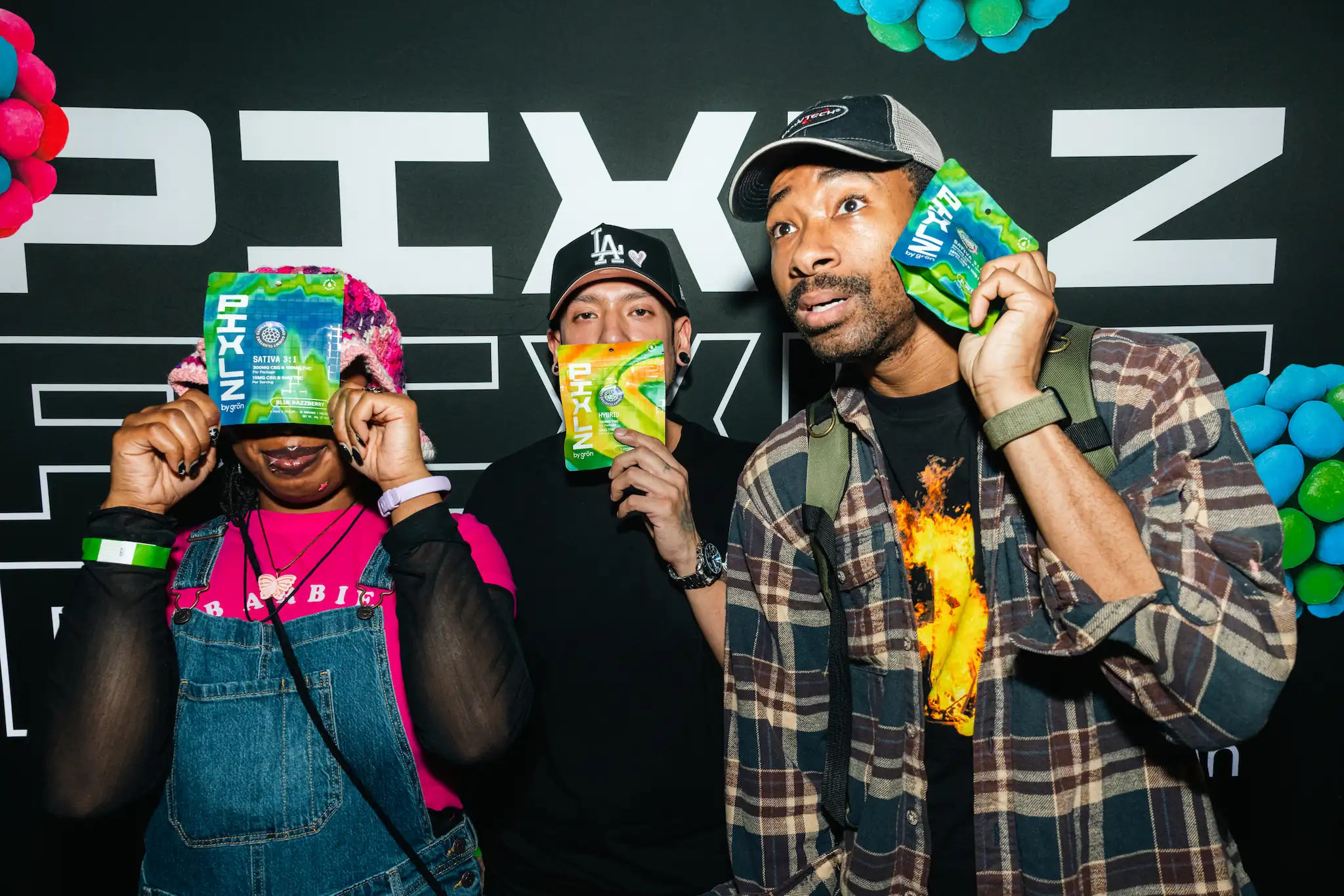 Three people holding colorful PIXLZ by grön product packages, posing in front of branded backdrop.