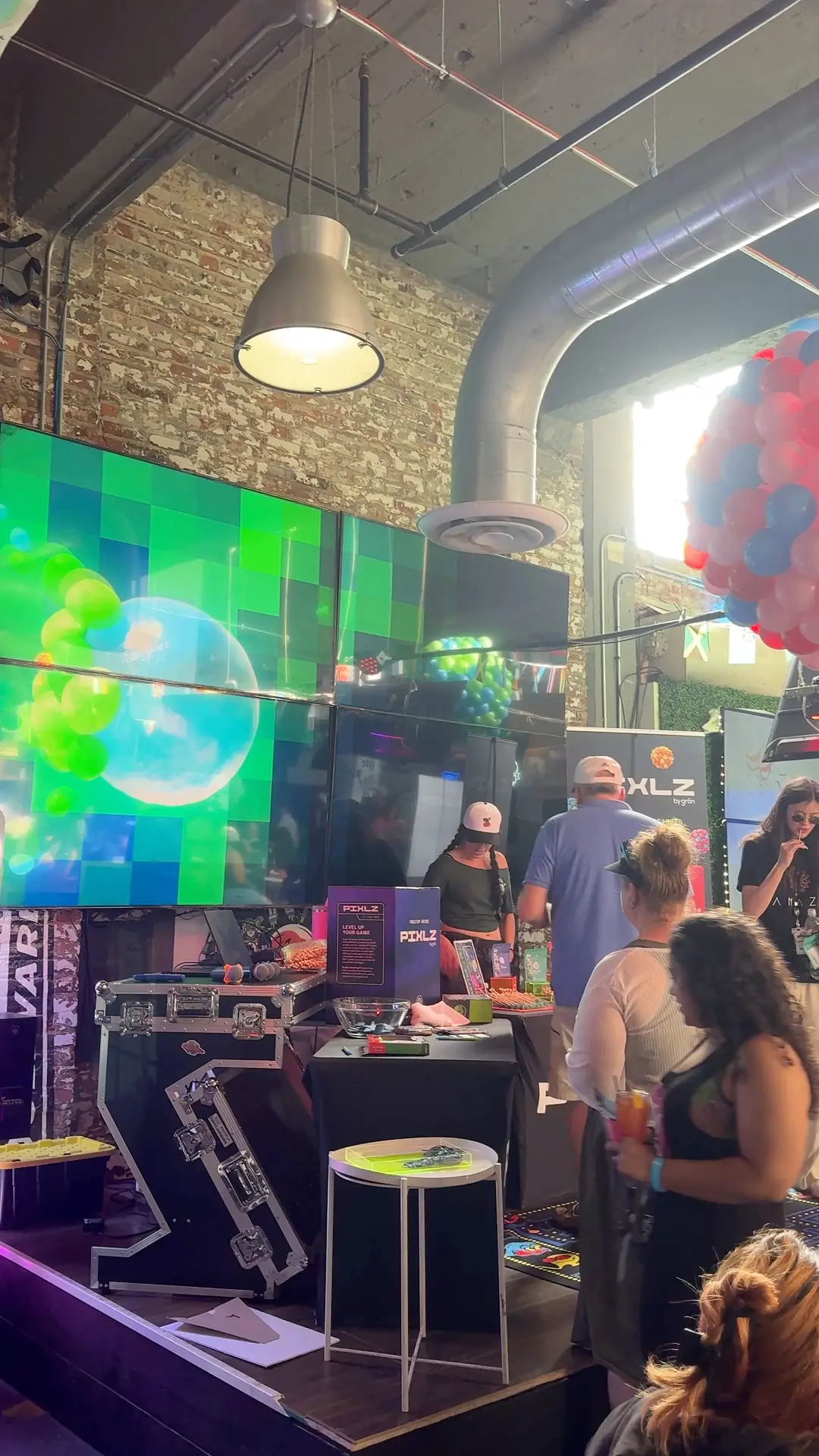 People inside a tent at an event with a retro Ms. Pac-Man arcade game and Pixlz display booth.