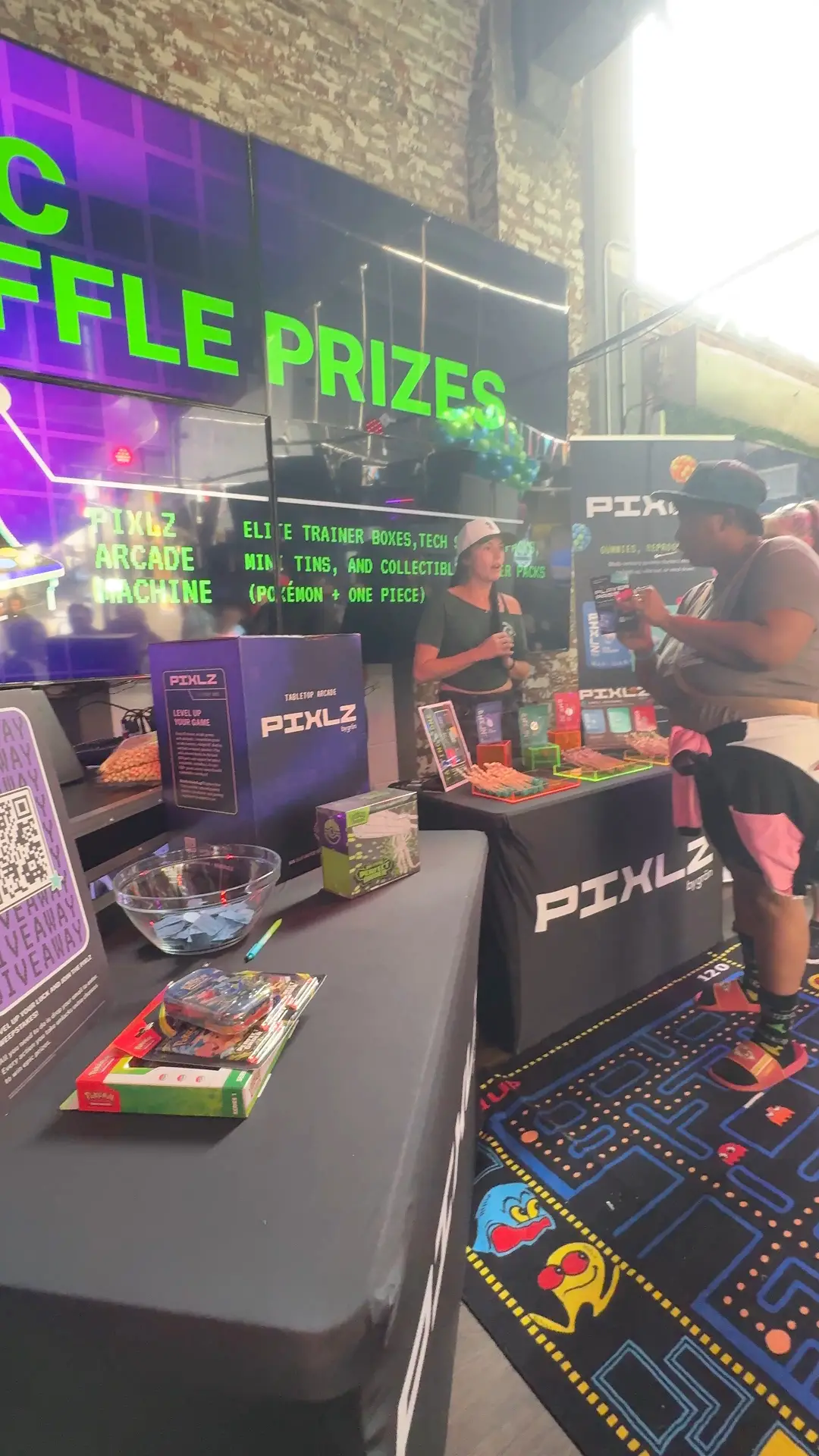 Person wearing black shirt with cartoon print and holding a colorful PIXLZ indica edible package.