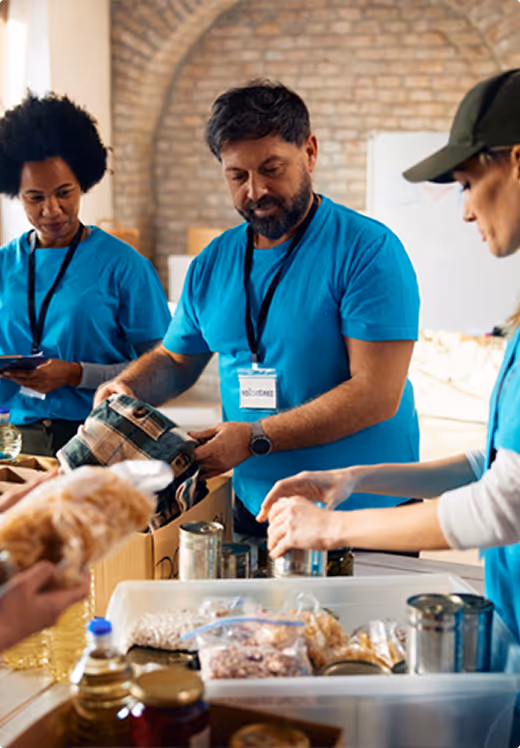 Volunteers in blue shirts sorting food items in boxes at a community food bank or charity event.