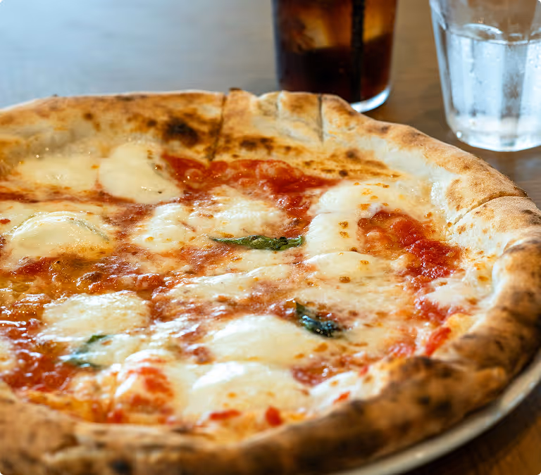 Pizza margherita with melted cheese, tomato sauce, and basil leaves on a rustic crust.